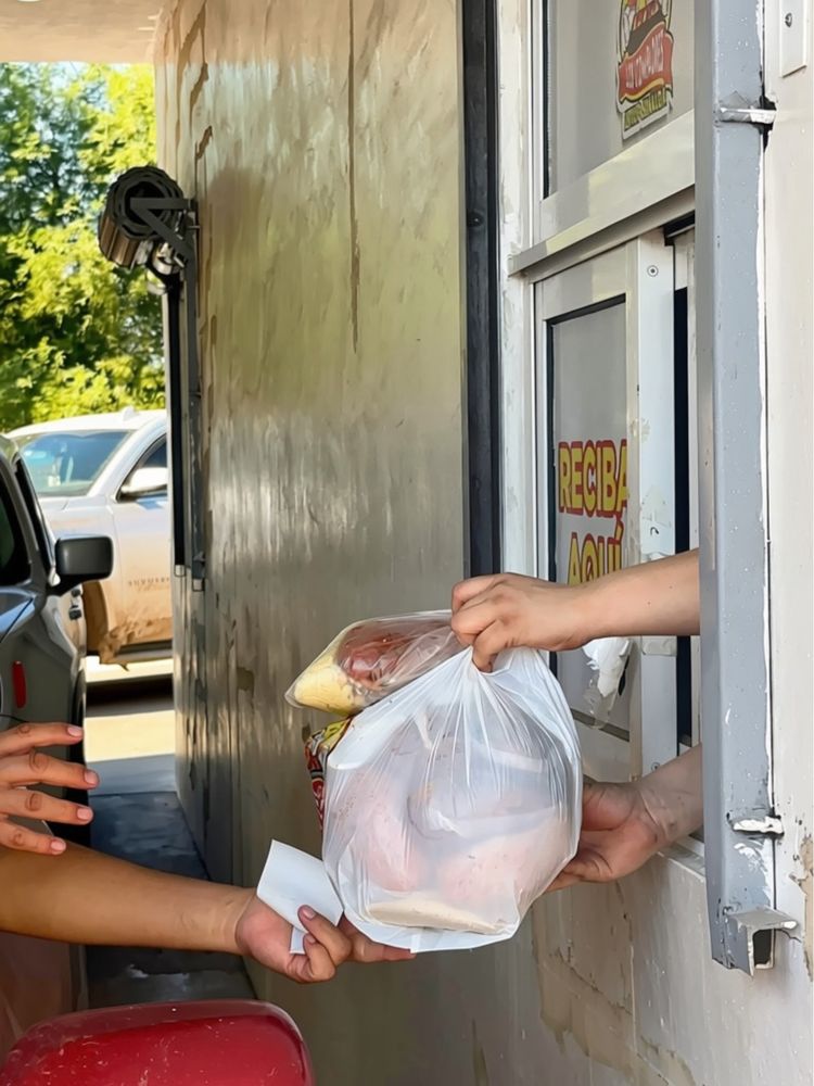 Entrega de un pedido por la ventanilla del Drive Thru; solo se ven manos