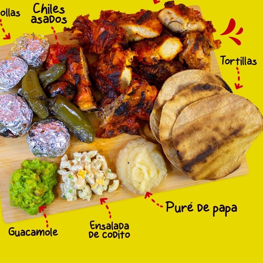 Tabla con pollo asado, chiles, cebollas en aluminio, tortillas, guacamole, ensalada de codito y puré de papa